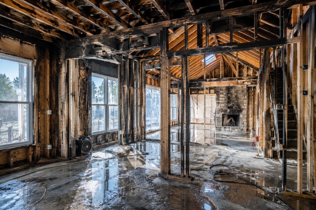 Fire-damaged home interior mid-restoration with exposed charred framing, drying equipment, and a stone fireplace